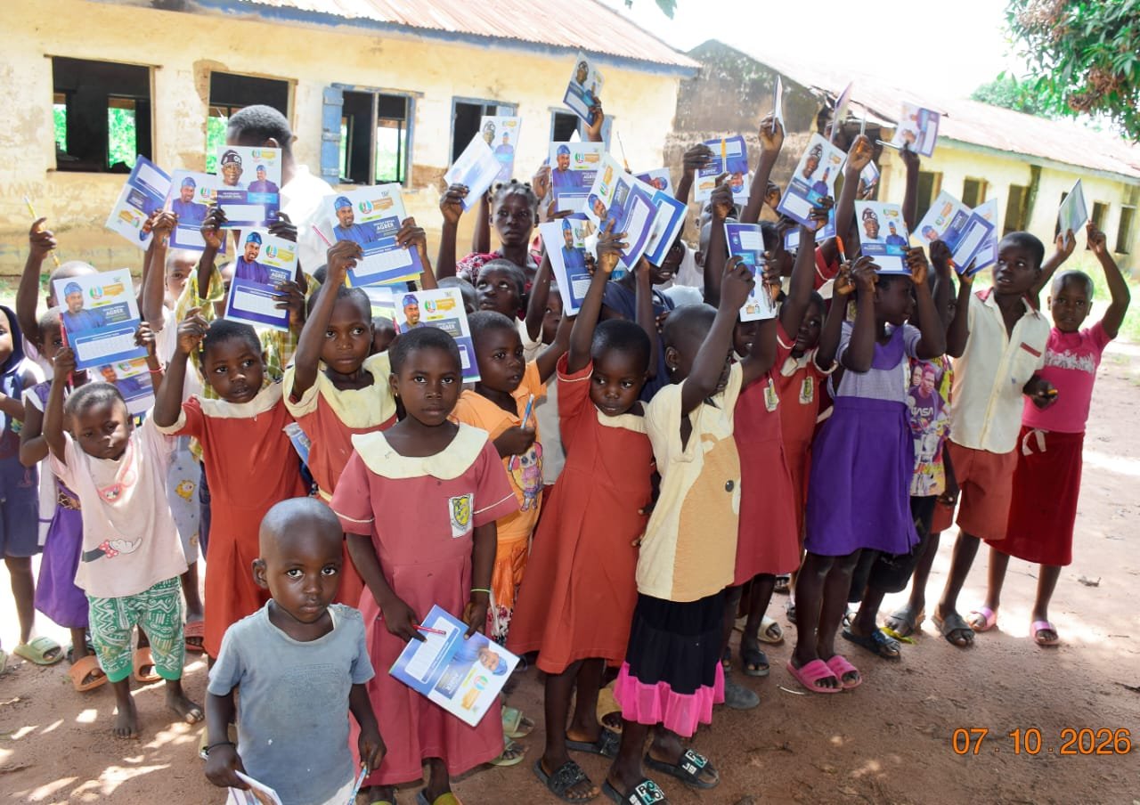 Girls in red and pink dresses holding branded exercise books in front of an older brown building
