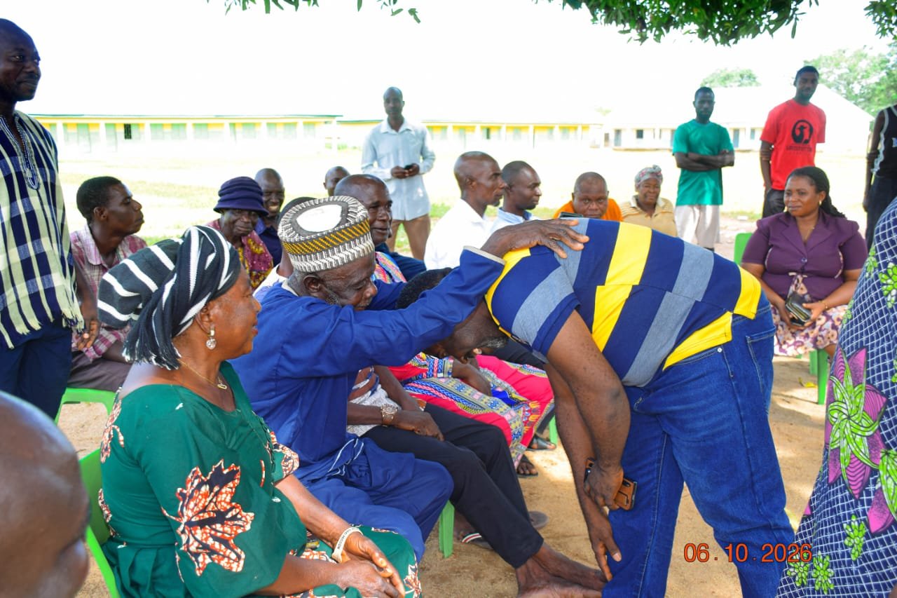Agber in a striped polo bowing to greet an elder in a patterned cap