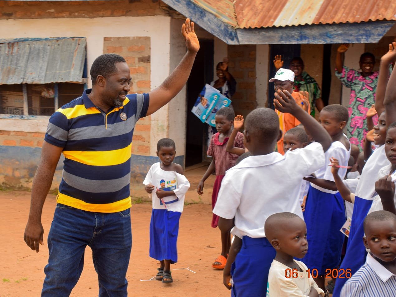 Agber in a striped polo high fiving a pupil at a school in Mbaakura Council Ward