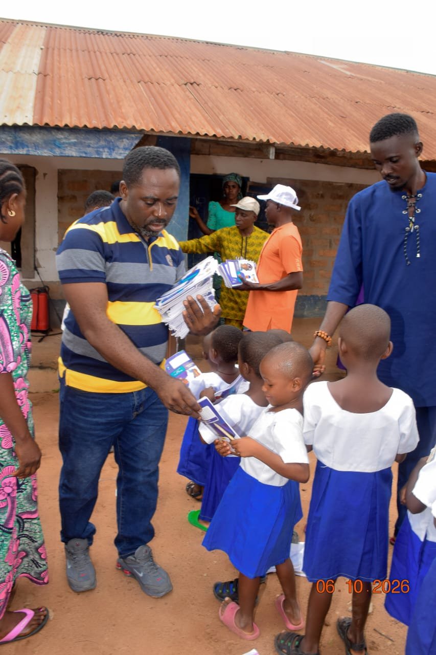 Agber handing exercise books to young girls at a school in Mbaakura